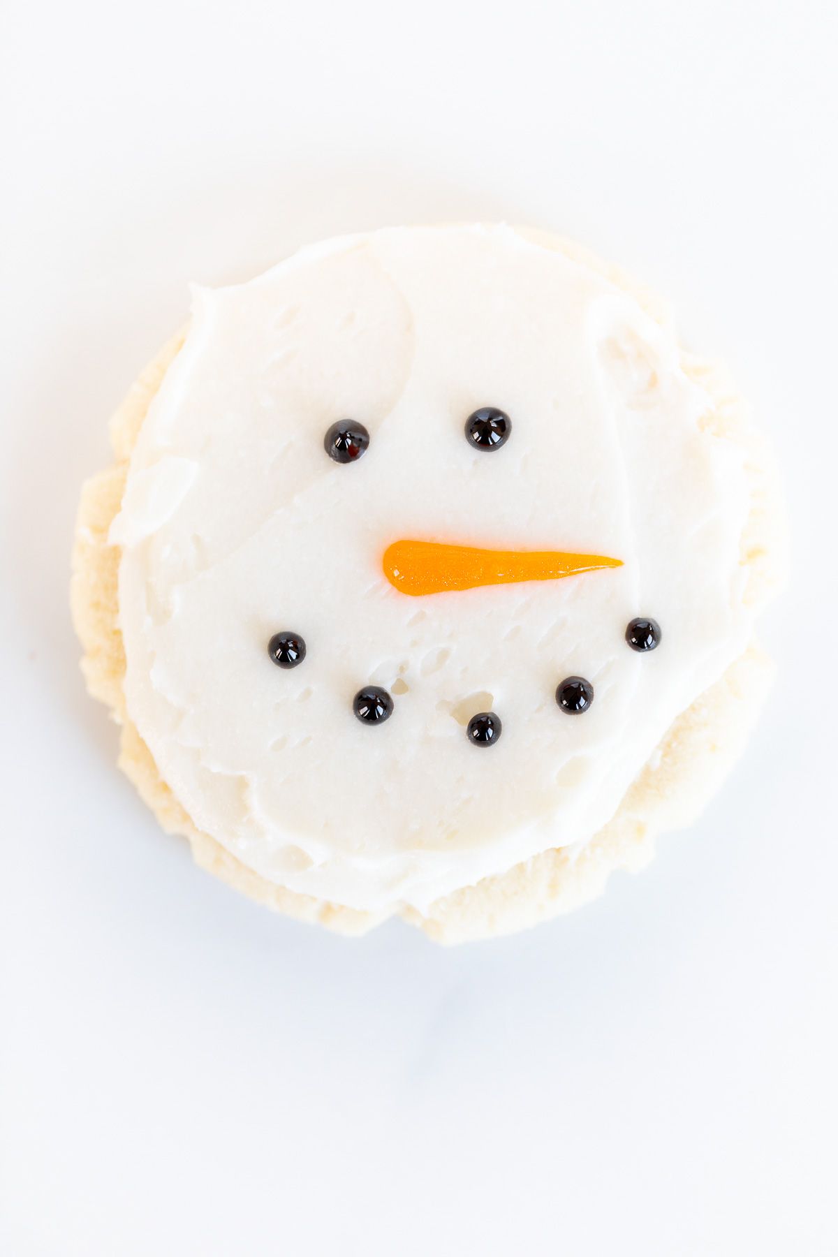 Round Christmas Sugar Cookie decorated with snowmen face on a marble surface.