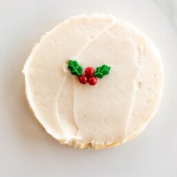 A single white frosted round Christmas Sugar cookie on a marble surface, single holly berry decoration in center.