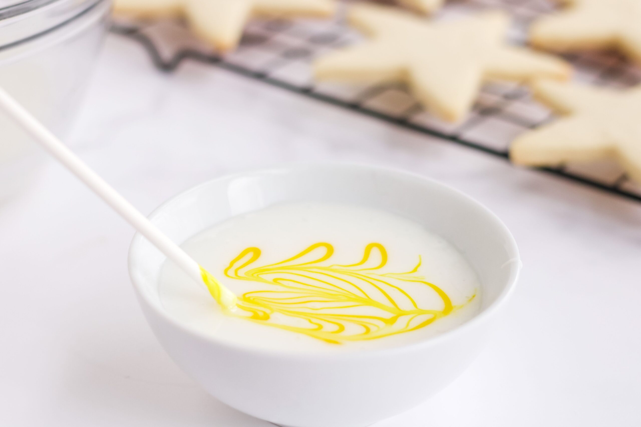 A bowl of white sugar cookie icing with yellow marbling.