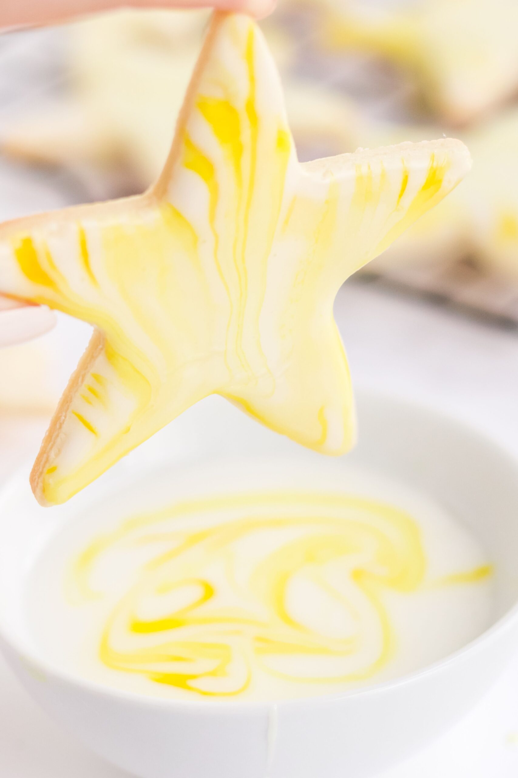 A sugar cookie with marbled icing in a star shape coming from a bowl of icing.