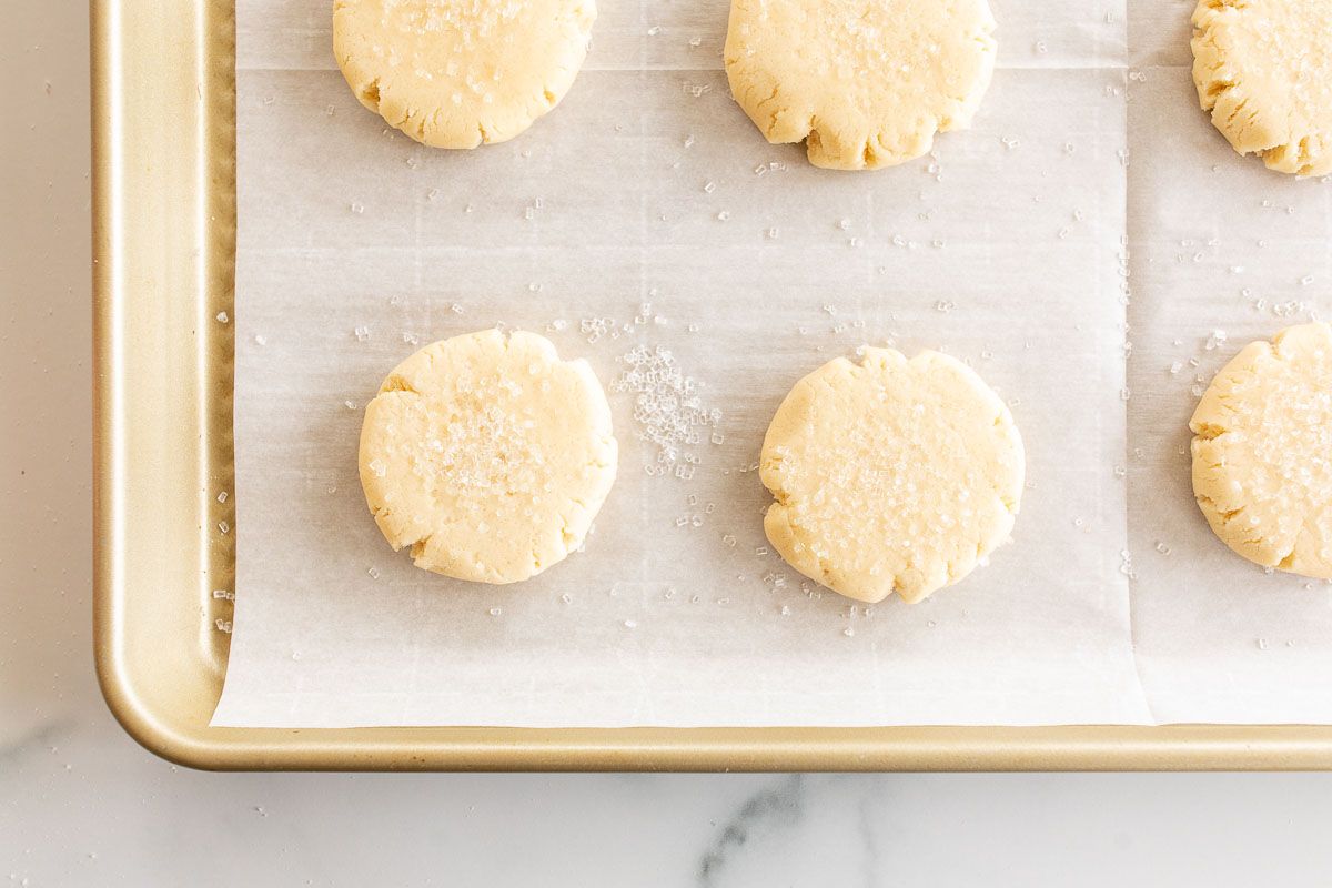 Simple round baked Christmas sugar cookies on a parchment lined gold baking sheet.
