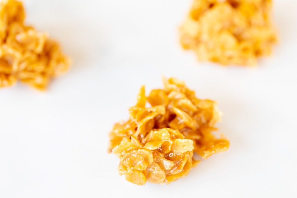 Three cornflake cookies on a white surface.