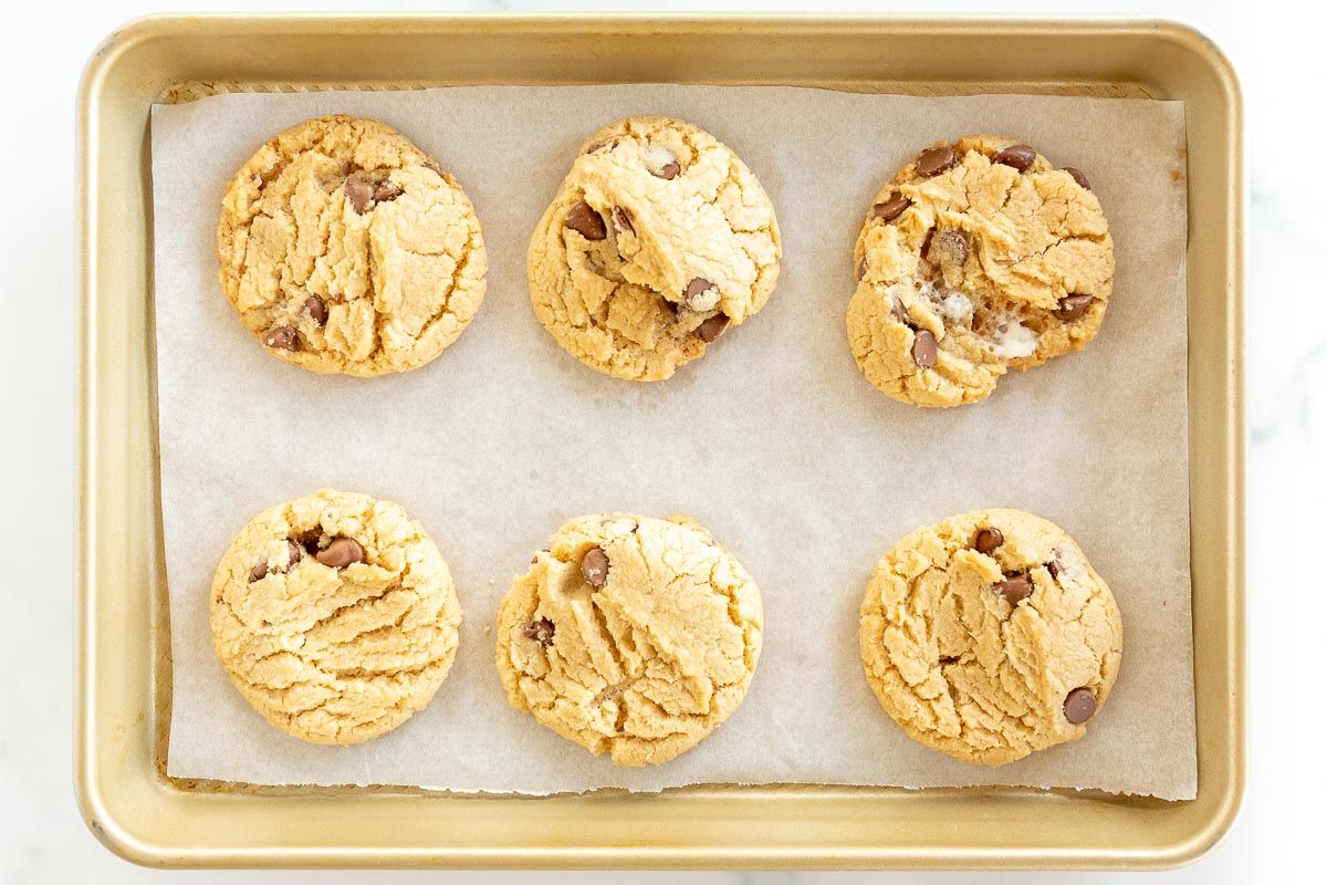 Six marshmallow cookies with chocolate chips on a gold baking sheet lined with parchment paper.