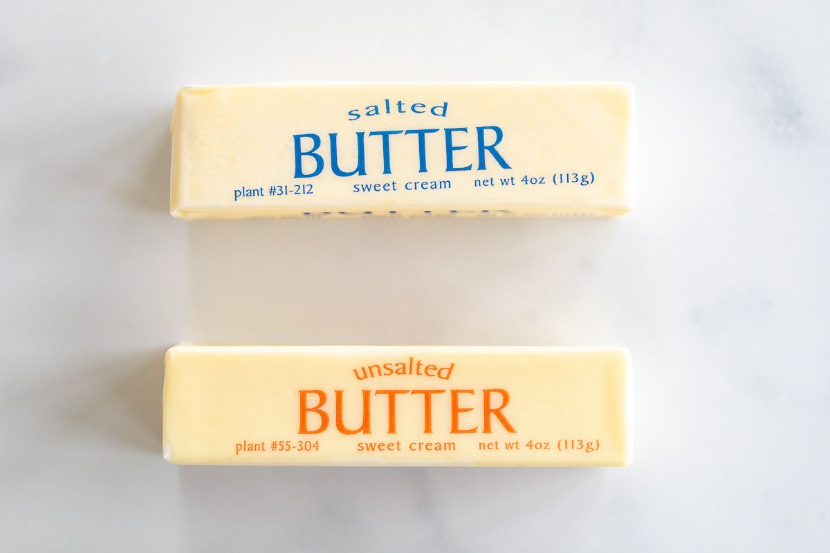 A stick of unsalted butter next to a stick of salted butter on a marble surface.