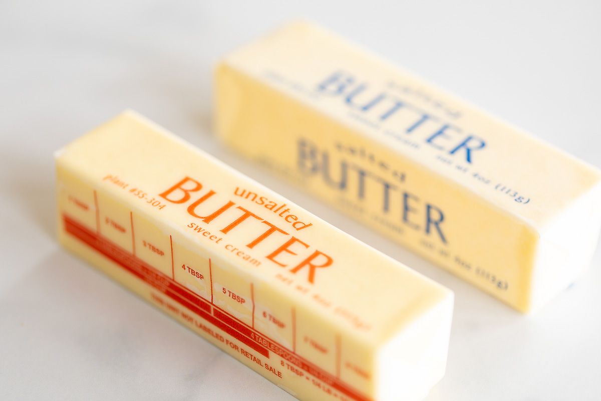 A stick of unsalted butter next to a stick of salted butter on a marble surface.