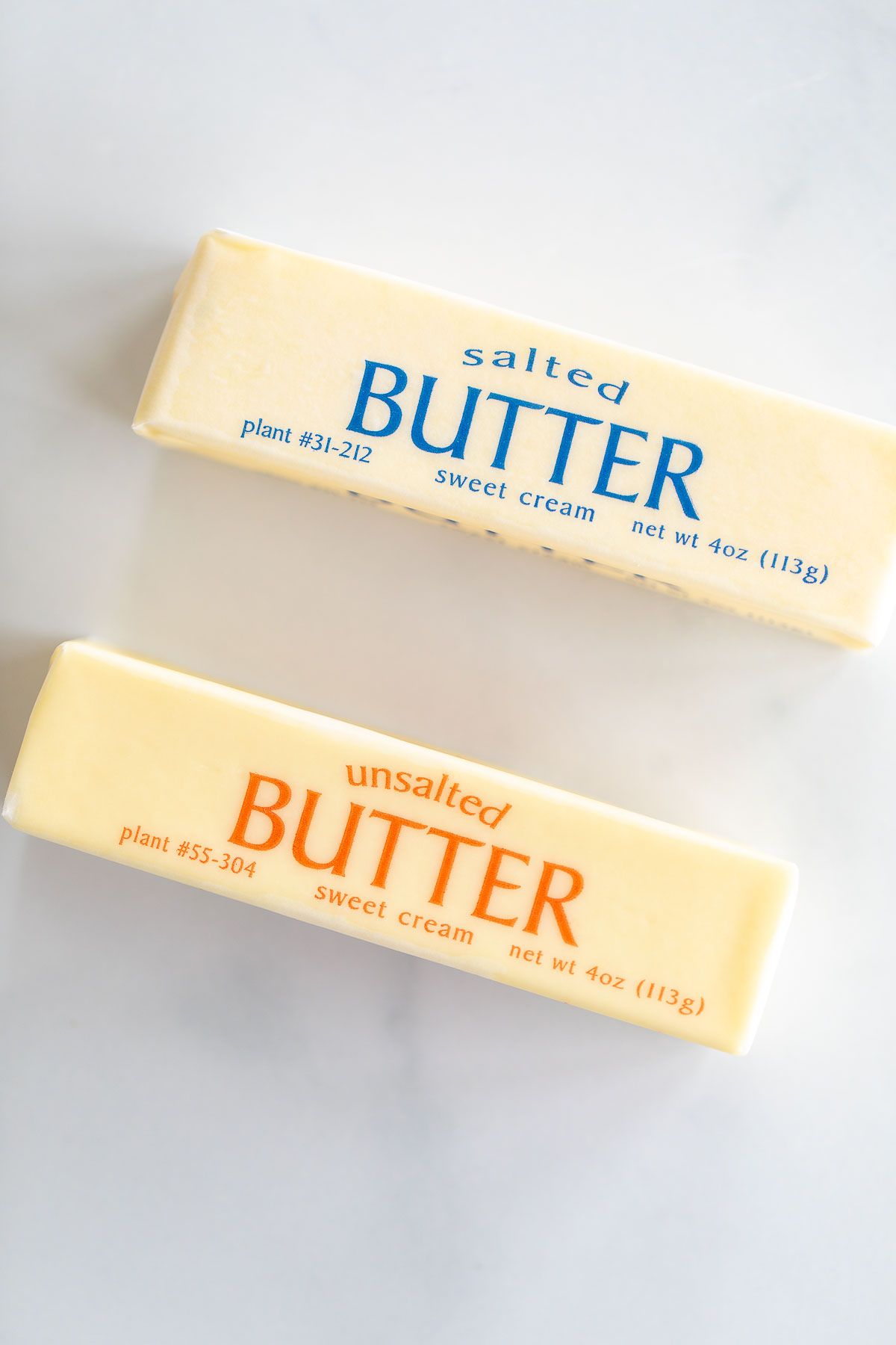 A stick of unsalted butter next to a stick of salted butter on a marble surface.