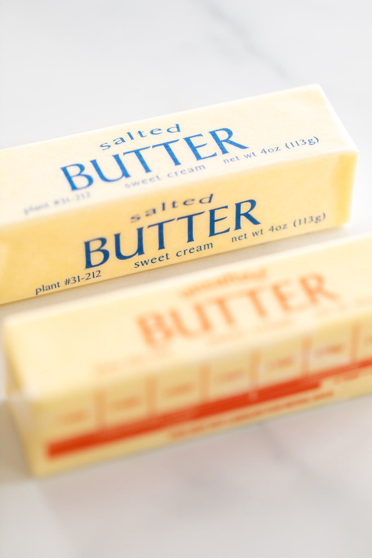 A stick of unsalted butter next to a stick of salted butter on a marble surface.