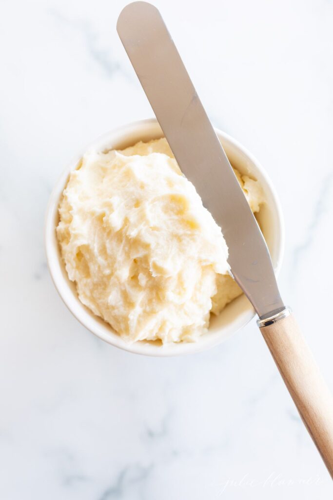 A bowl of lemon frosting on a marble surface, spreading knife resting on top.