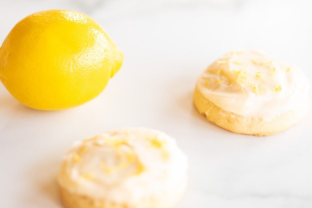 Frosted lemon cookies on a marble surface, whole lemon in the background