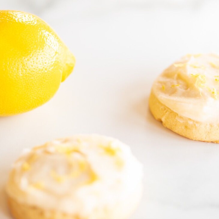 Frosted lemon cookies on a marble surface, whole lemon in the background