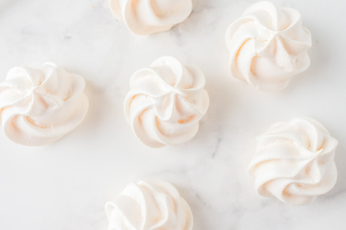 Pale pink and white meringues on a marble surface.