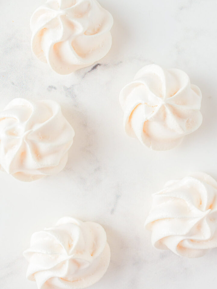 Pale pink and white meringues on a marble surface.