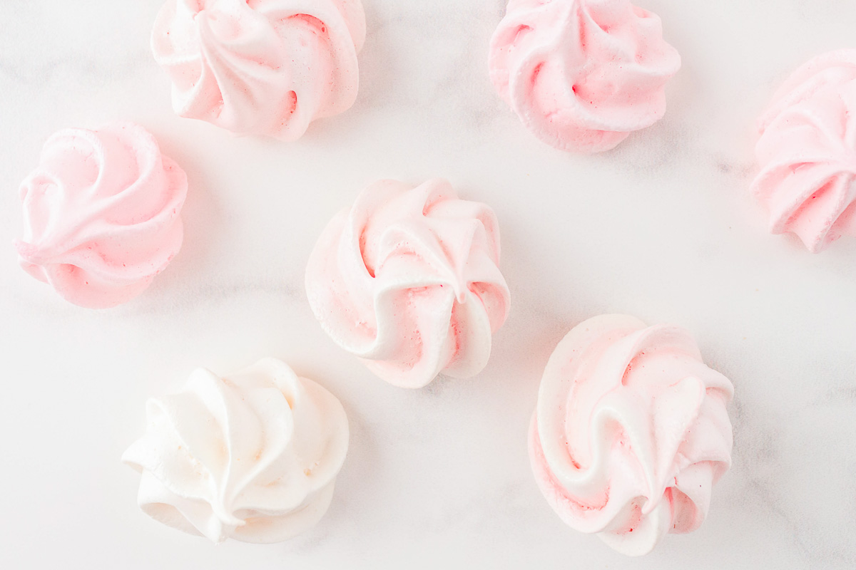 Pale pink and white meringues on a marble surface.
