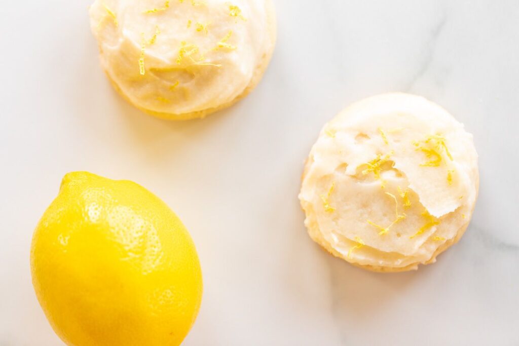 Frosted lemon cookies on a marble surface, whole lemon in the background