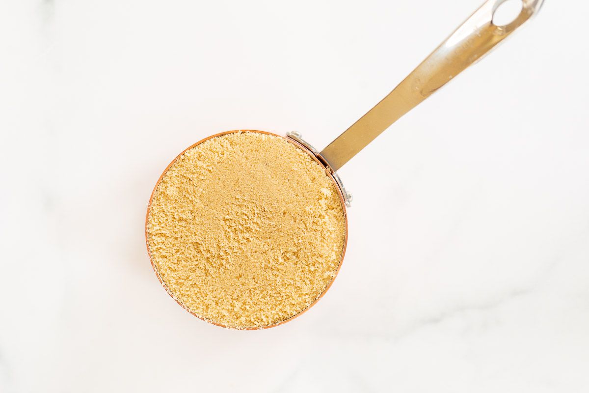 A measuring scoop filled with light brown sugar on a marble surface.