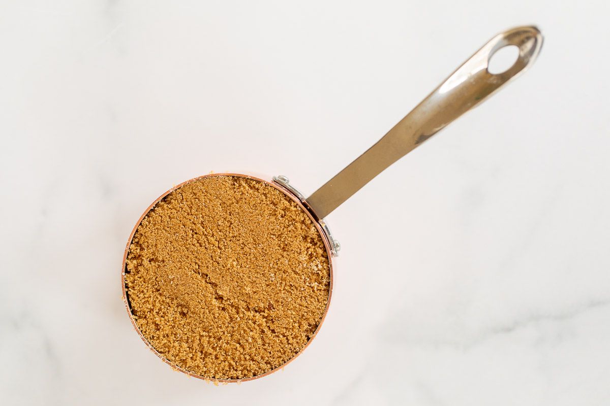 A measuring scoop filled with dark brown sugar on a marble surface.