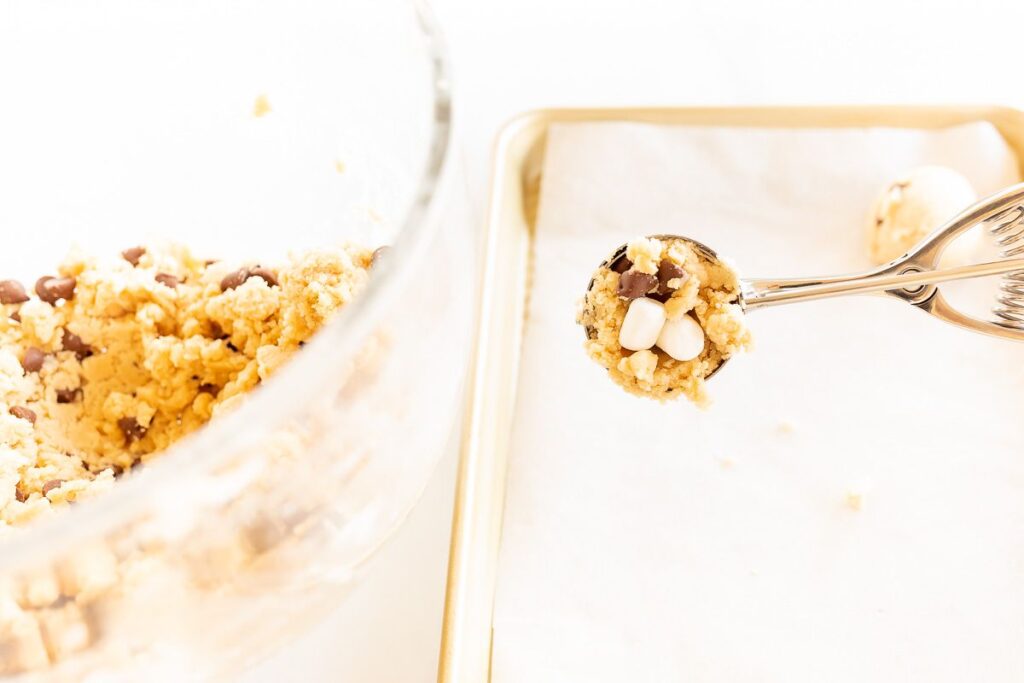 A cookie scoop, scooping cookie dough onto a baking sheet lined with parchment