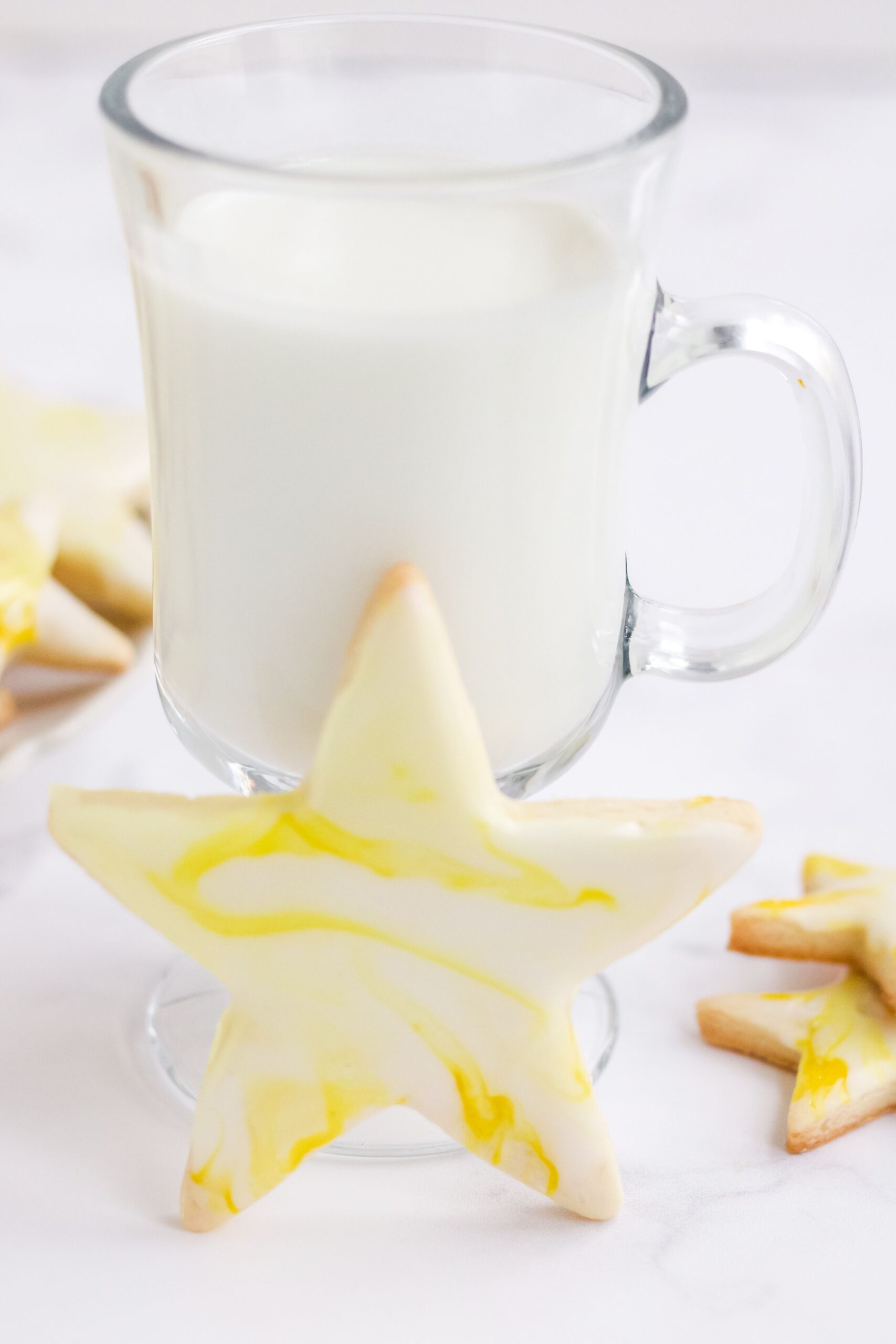 Star shaped cutout sugar cookies topped with yellow marbled royal icing in front of a mug of milk.