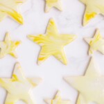 Star shaped cutout sugar cookies topped with yellow marbled royal icing, spread out on a marble surface.