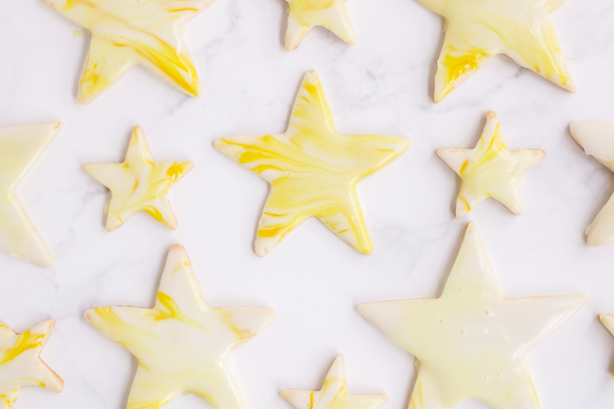 Star shaped cutout sugar cookies topped with yellow marbled royal icing, spread out on a marble surface.