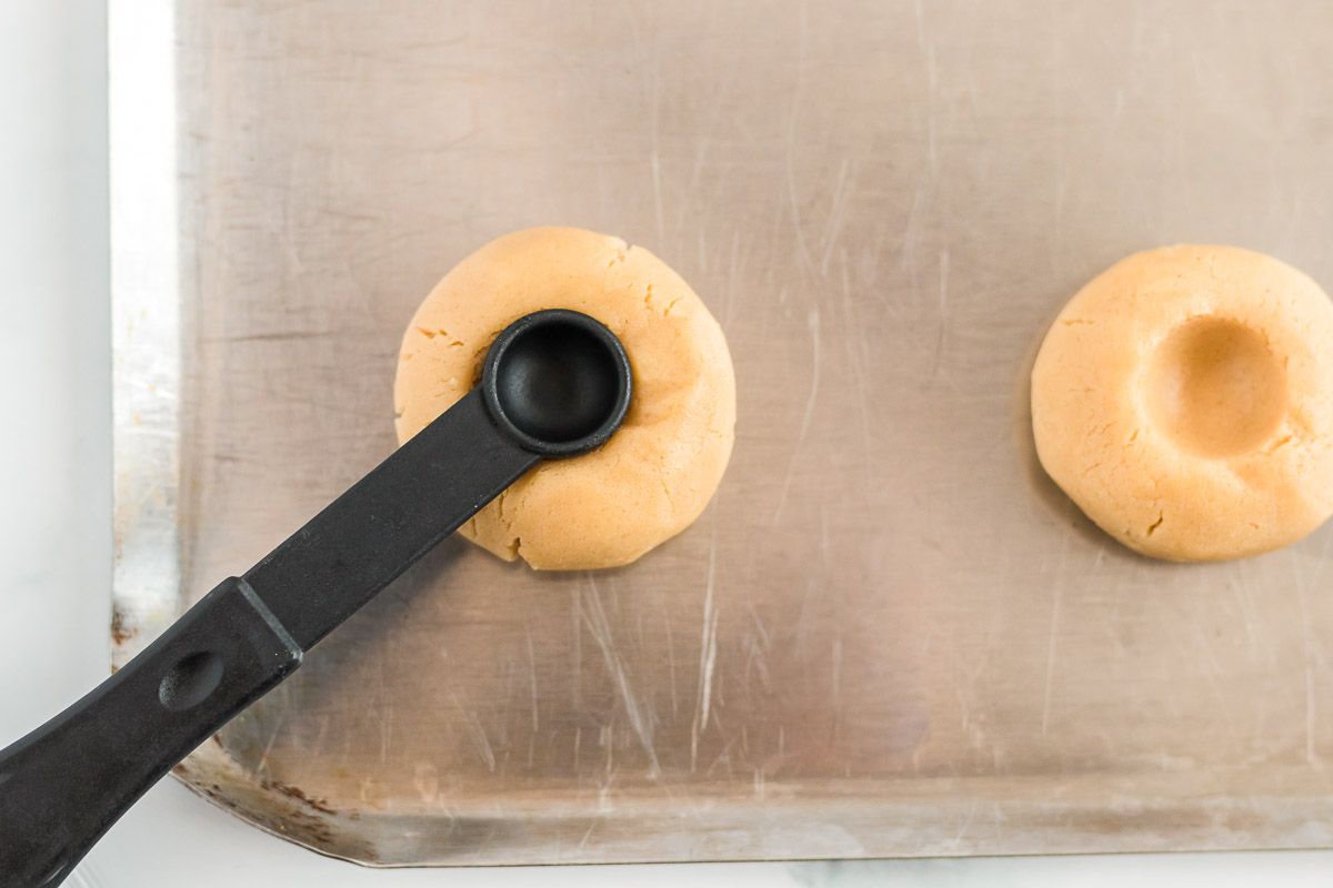 A tablespoon pressing into a cookie on a baking sheet to create an indent.