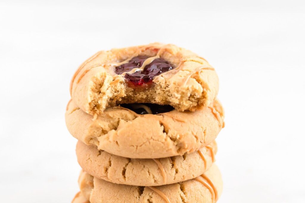 A stack of peanut butter and jelly cookies on a white background, top one has a bite missing.