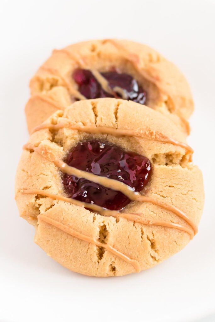 Two homemade peanut butter and jelly cookies on a white surface.
