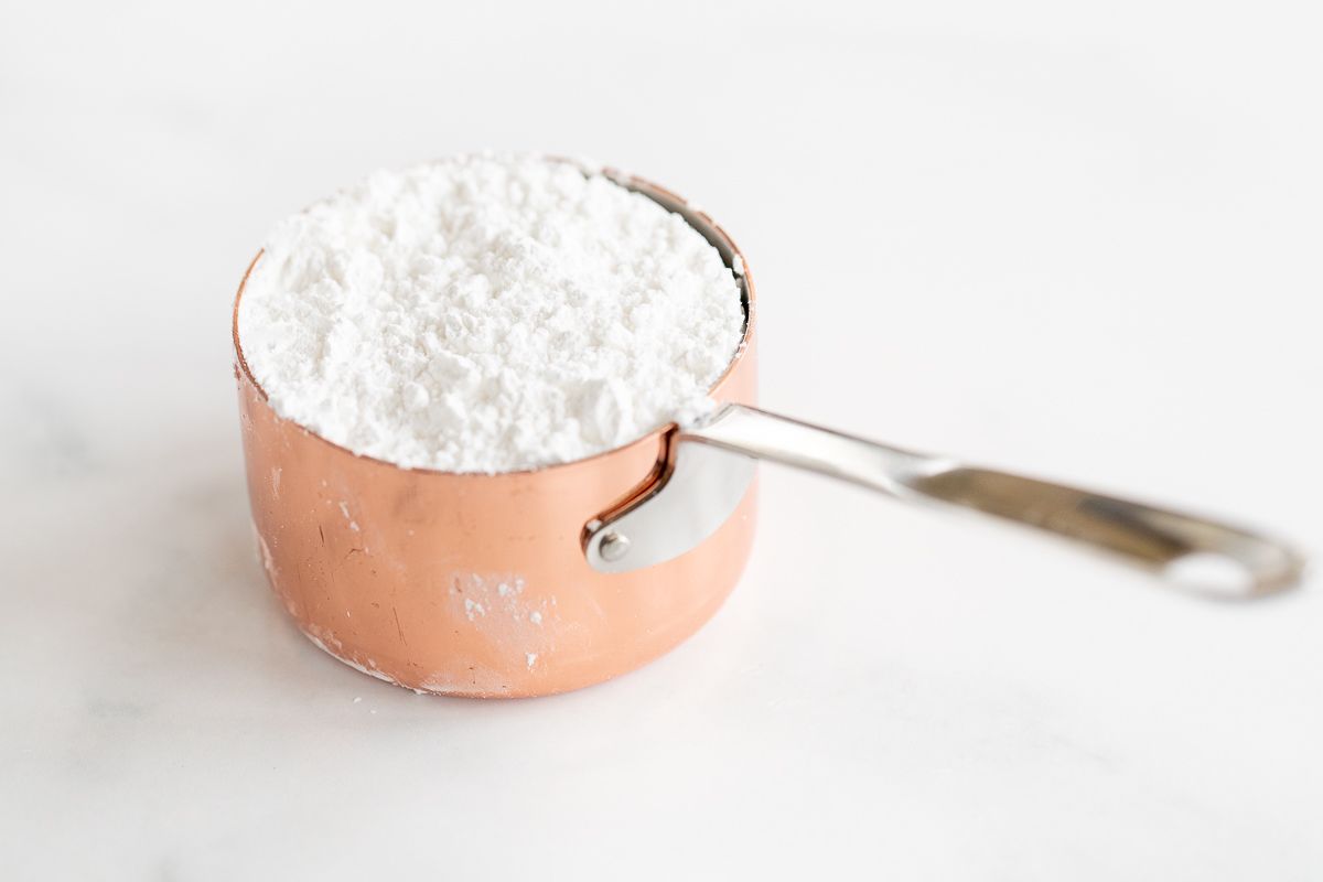 copper measuring cup with metal handle filled with powdered sugar