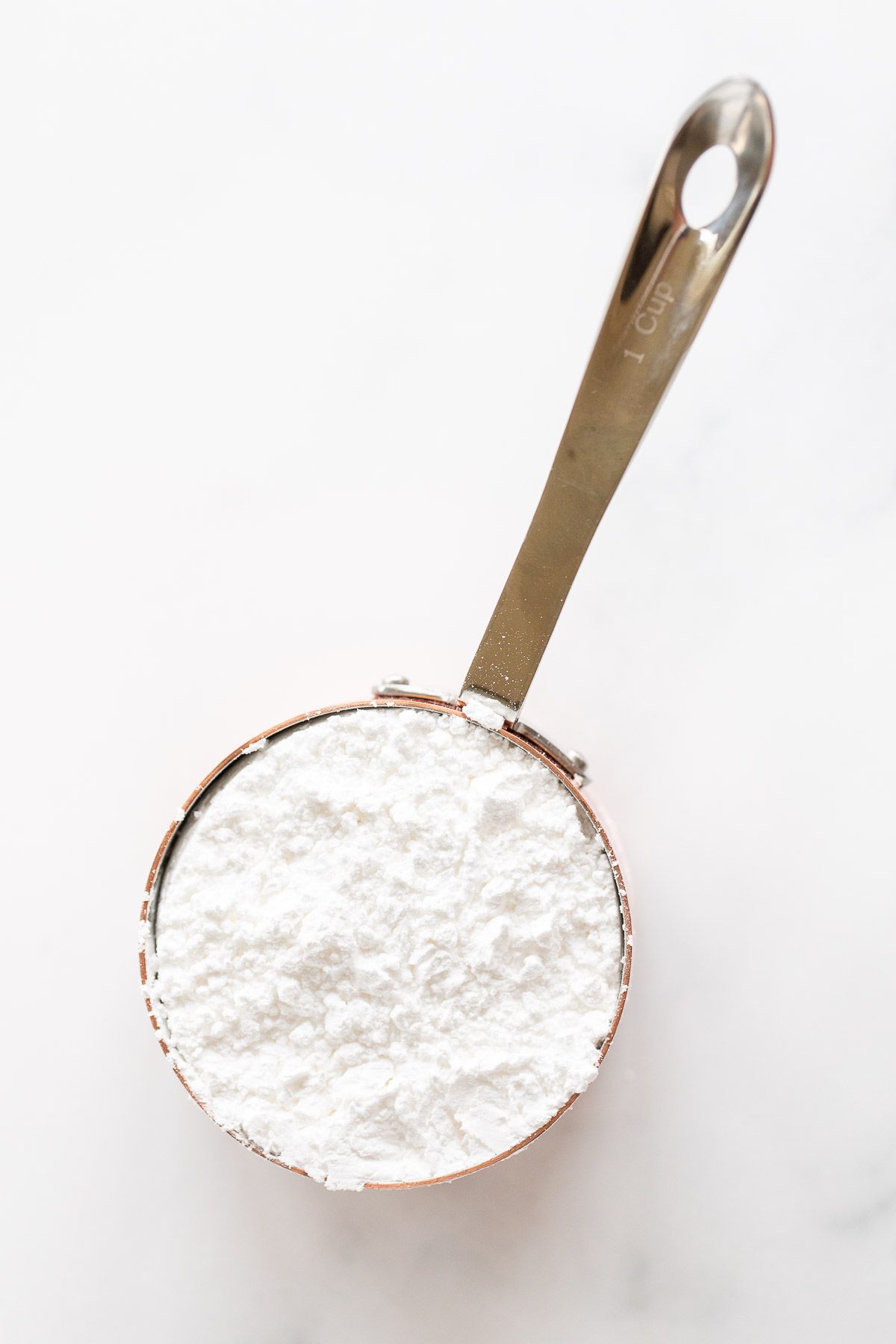 powdered sugar in a copper measuring cup sitting on a marble countertop