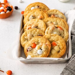Halloween cookies with M&Ms in a small silver tray lined with parchment. Gray towel to the side.