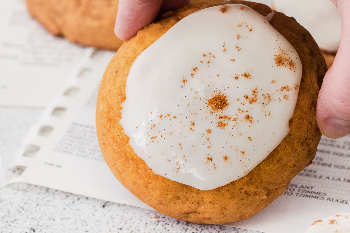 A pumpkin cookie with white frosting, sprinkled with nutmeg