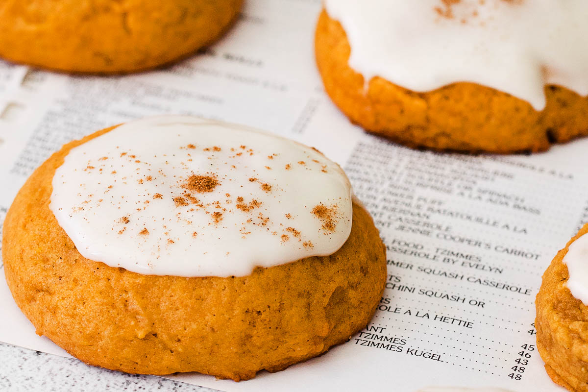 Pumpkin cookies with cream cheese frosting on a white countertop