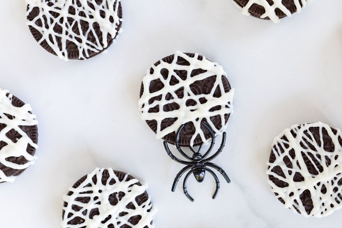 oreo spider cookies laid out on a white surface with a black plastic spider nearby