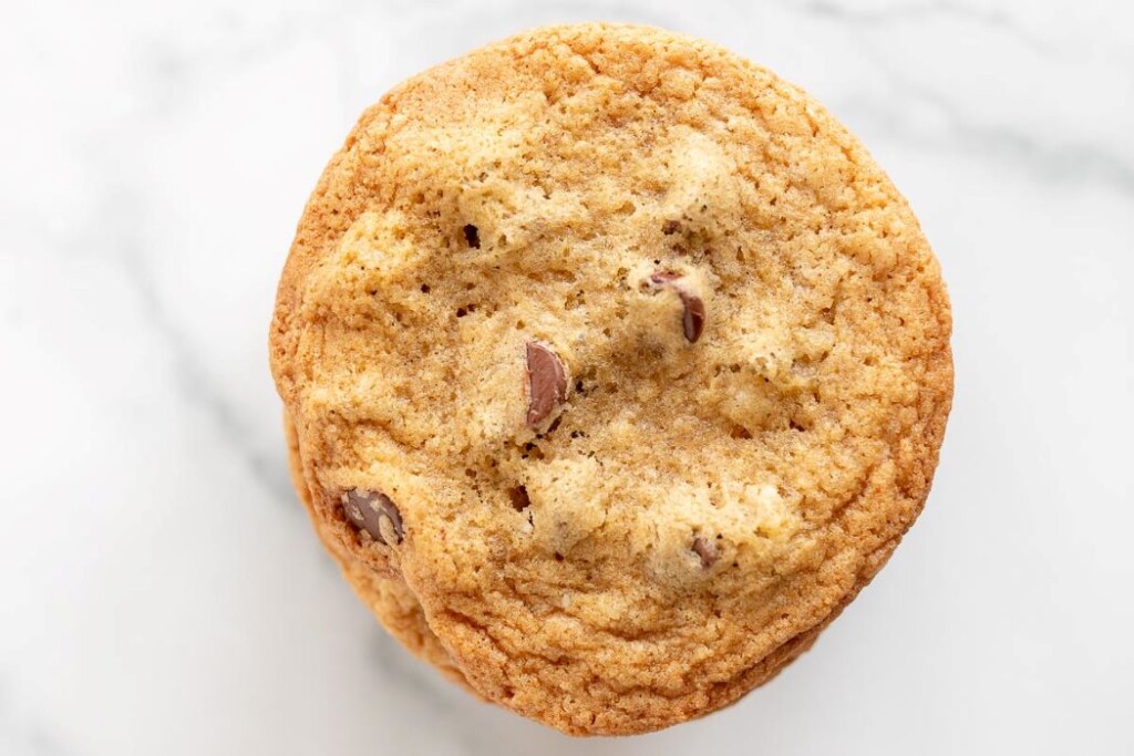 A single thin chocolate chip cookie on a marble surface