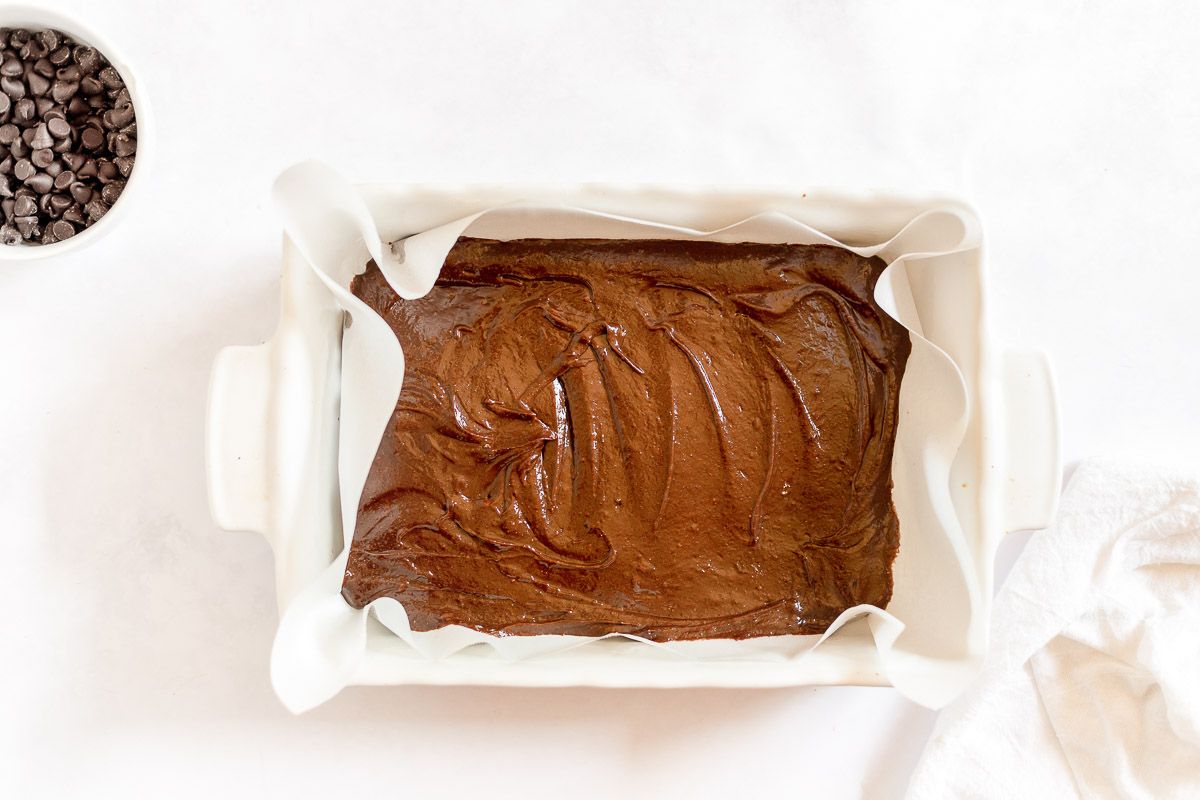 brownie batter in a white baking pan lined with parchment
