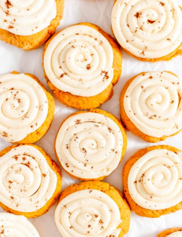 Pumpkin cake cookies on white parchment paper, topped with cream cheese frosting