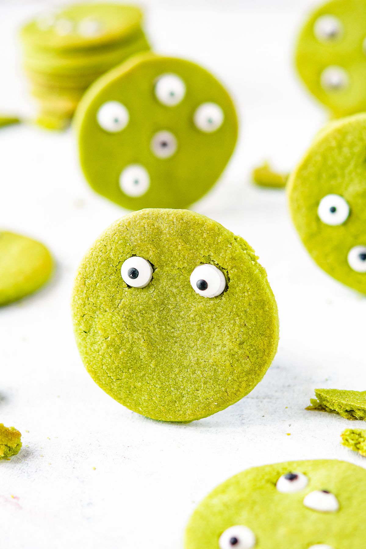 A round green Halloween Matcha cookie against a white background. Edible eyes decorate the cookie to look like a green monster face.