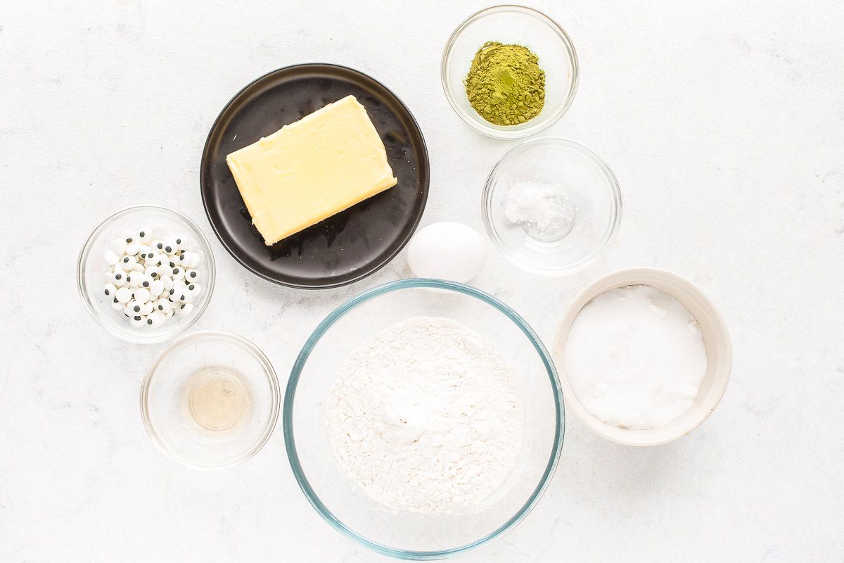 Ingredients for matcha cookies laid out in glass bowls on a white surface