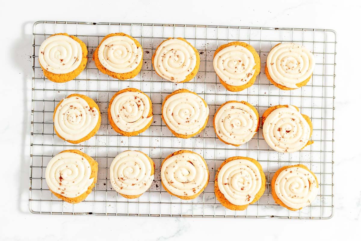 Pumpkin cake cookies on a wire cooling rack, topped with cream cheese frosting
