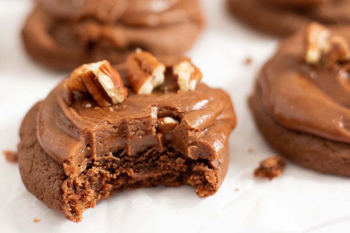 Texas sheet cake cookies topped with chopped pecans on a white surface, bite taken out of one