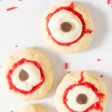 Eyeball cookies with red frosting and sprinkles, on a white surface