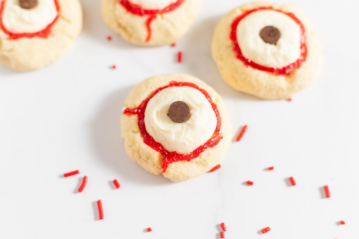 Eyeball cookies with red frosting and sprinkles, on a white surface