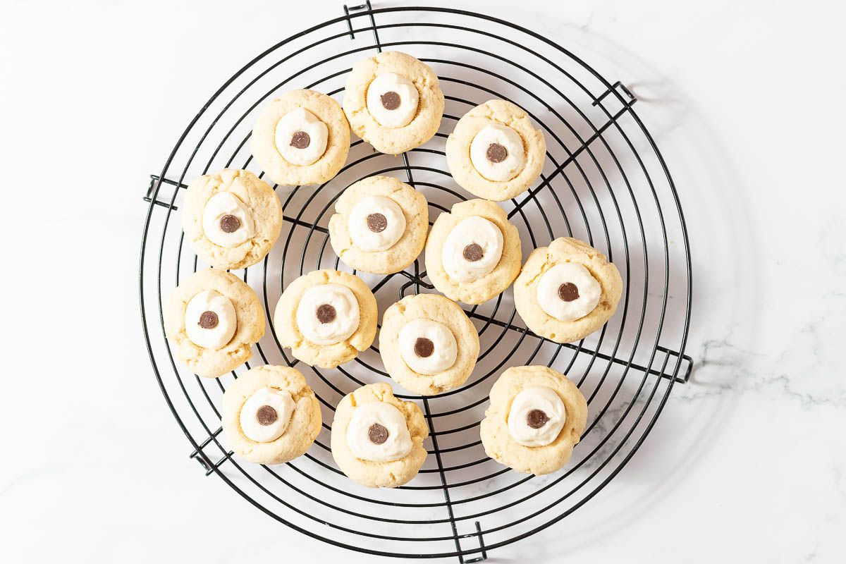 A round black wire cookie rack, with eyeball cookies being decorated on top