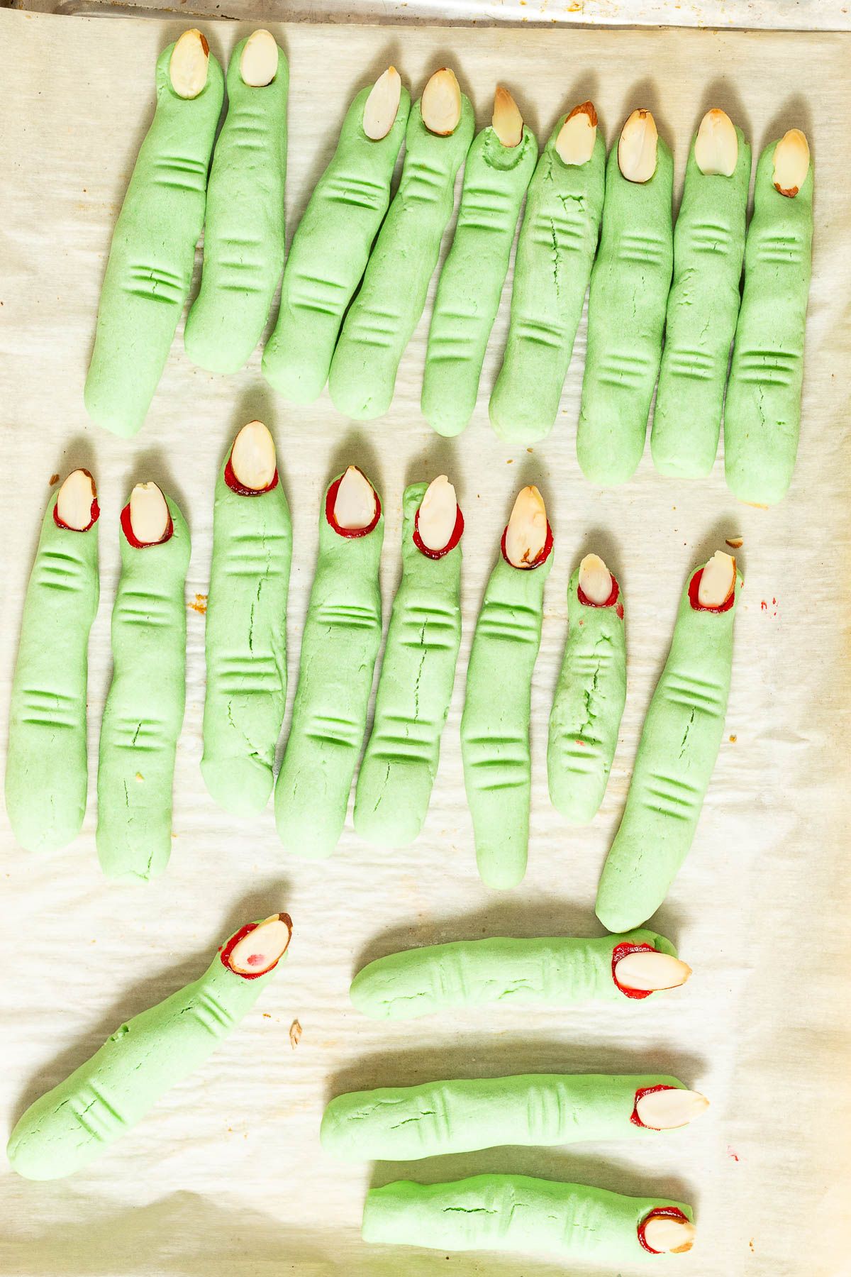 Green witch finger cookies on white parchment paper, on a cookie sheet after baking