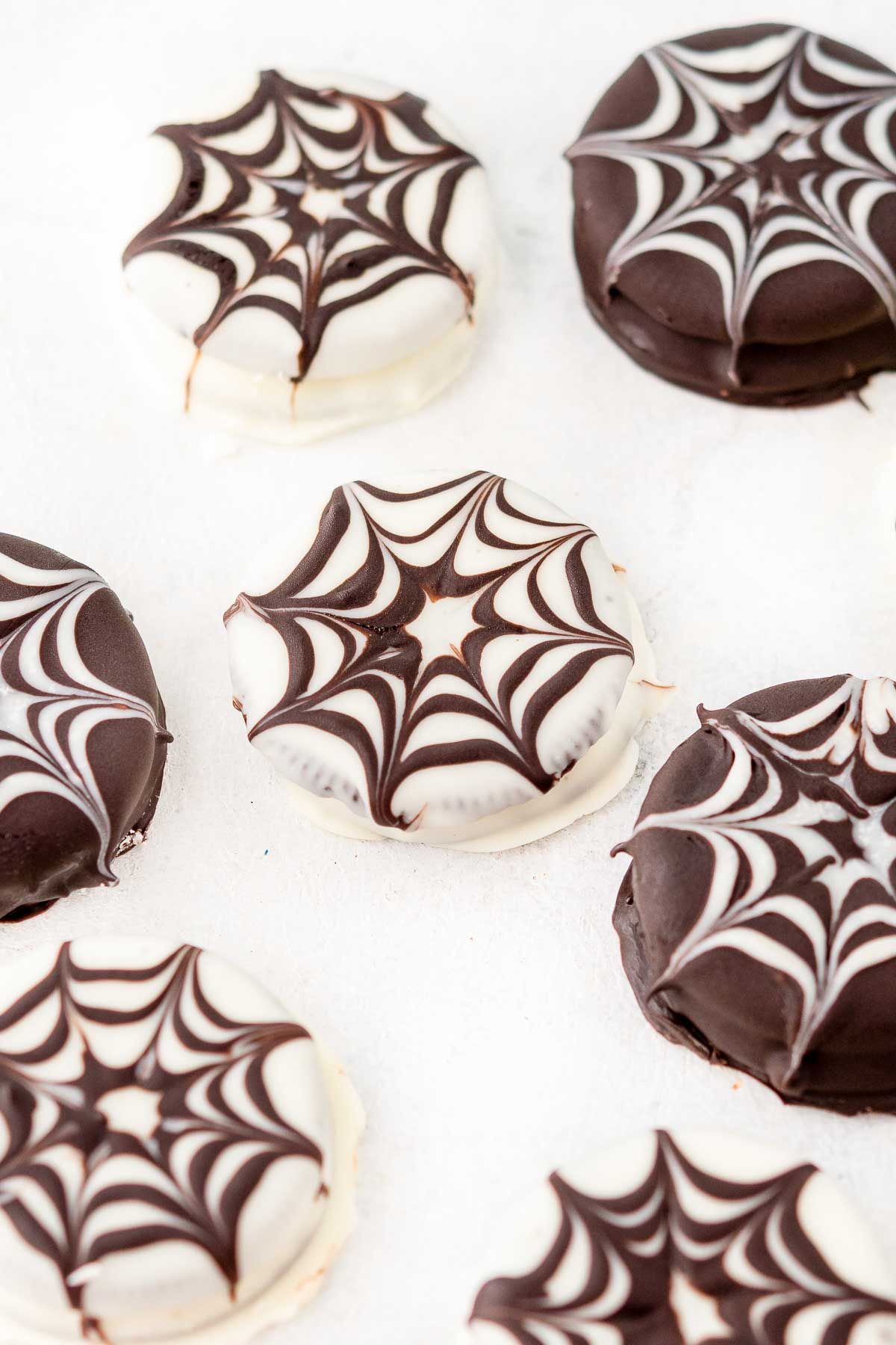 Halloween chocolate covered oreos made into spiderwebs, on a white surface.