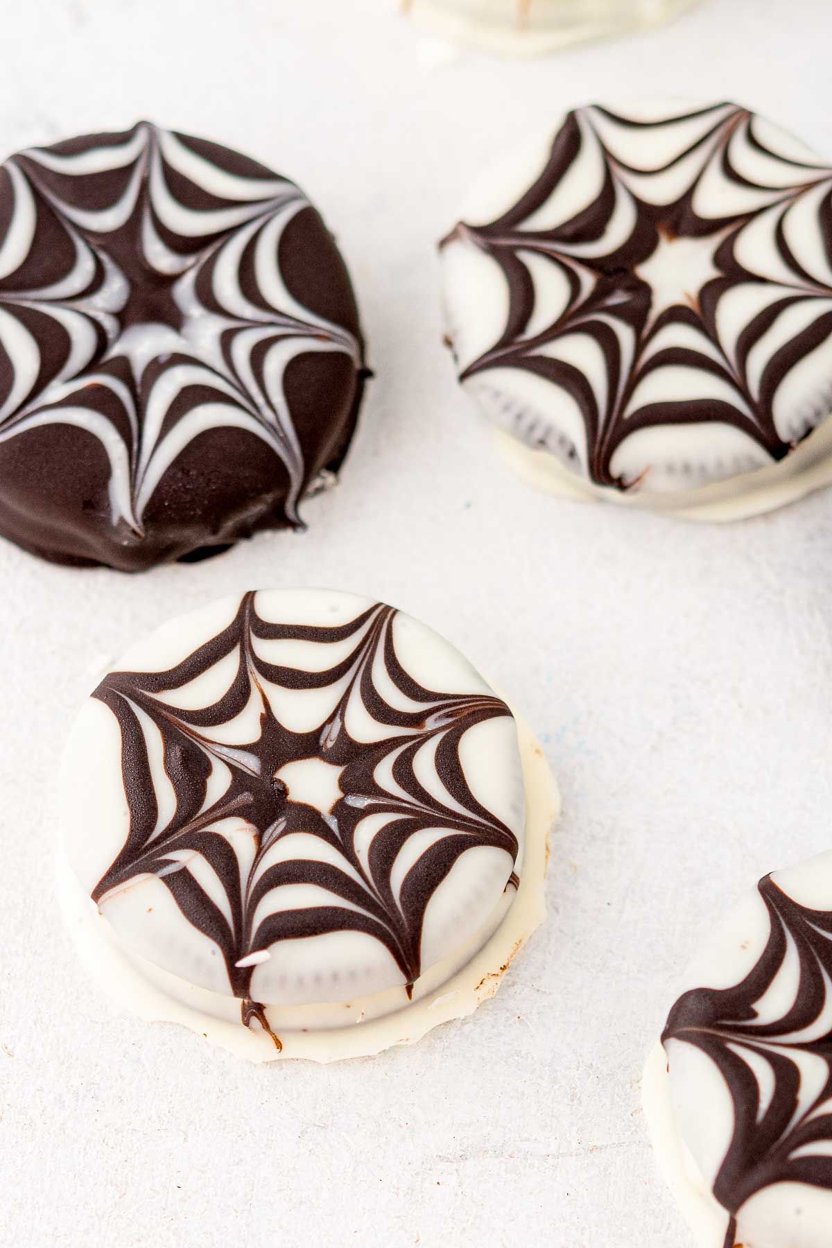 Halloween chocolate covered oreos made into spiderwebs, on a white surface.