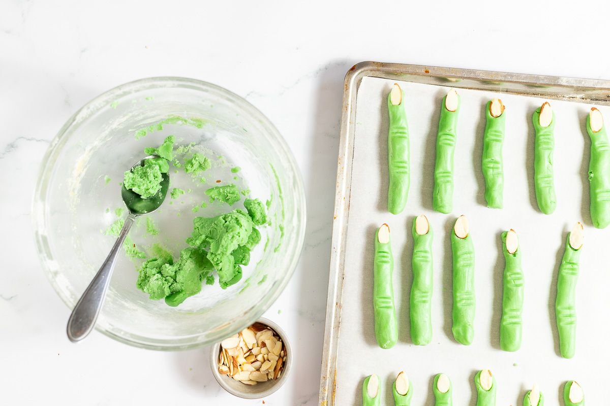 Green witch finger cookies on white parchment paper, on a cookie sheet before baking