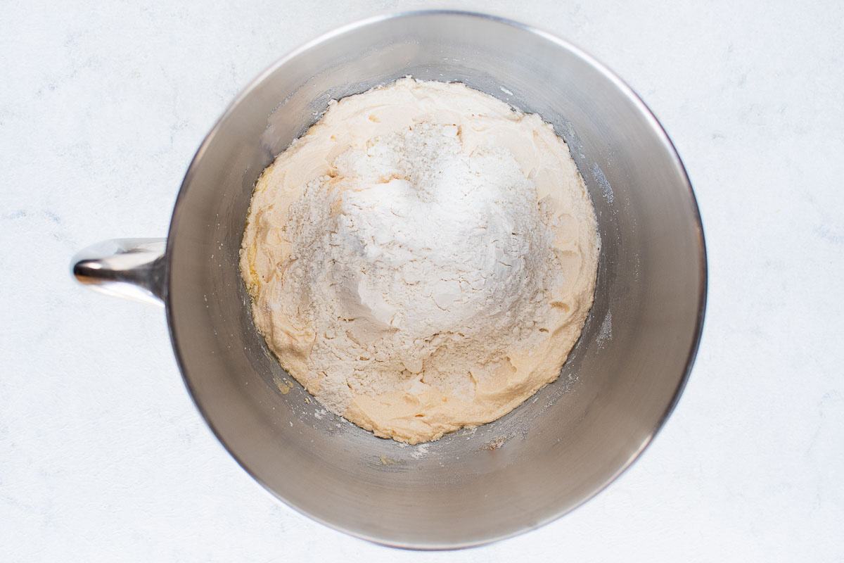 The bowl of a stand mixer filled with ingredients for cookie dough.