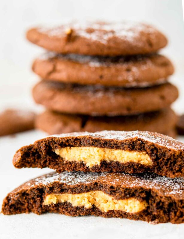 Two peanut butter filled brownie cookie halves stacked on top of each other with four stacked cookies in background