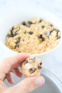 Hand holding tahini chocolate chip energy ball in front of bowl of dough